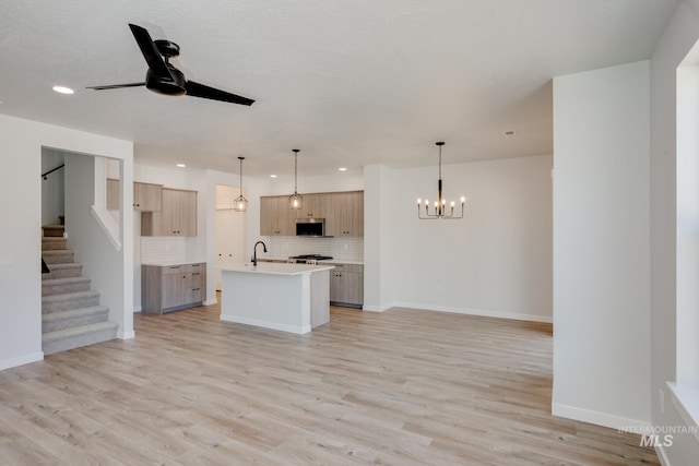 unfurnished living room with light wood-type flooring, baseboards, stairway, and ceiling fan with notable chandelier