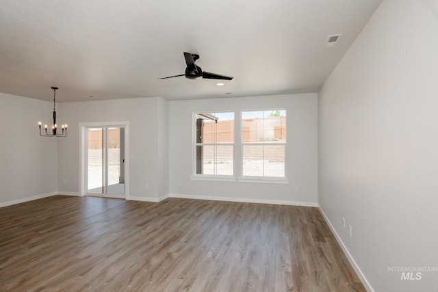 empty room featuring visible vents, light wood-style flooring, baseboards, and ceiling fan with notable chandelier