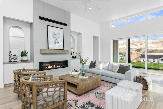 living room featuring a towering ceiling, light wood-type flooring, and a large fireplace