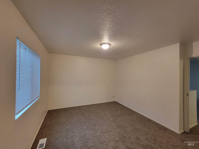 empty room with a wealth of natural light, visible vents, a textured ceiling, dark colored carpet, and baseboards