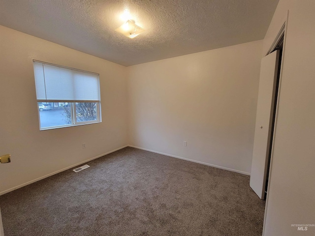 empty room featuring baseboards, visible vents, dark carpet, and a textured ceiling