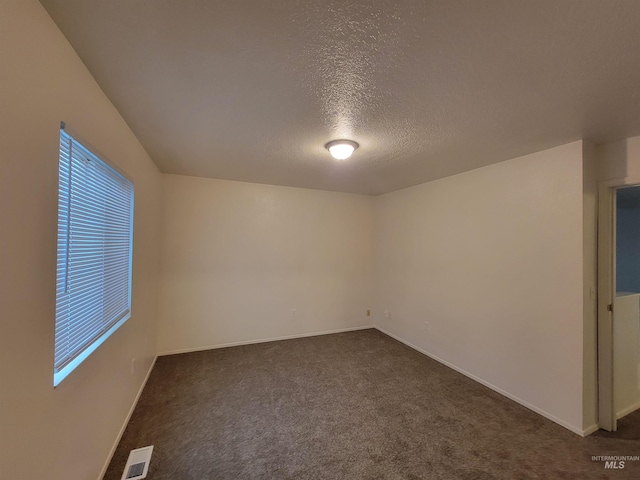 spare room with a wealth of natural light, visible vents, a textured ceiling, dark colored carpet, and baseboards