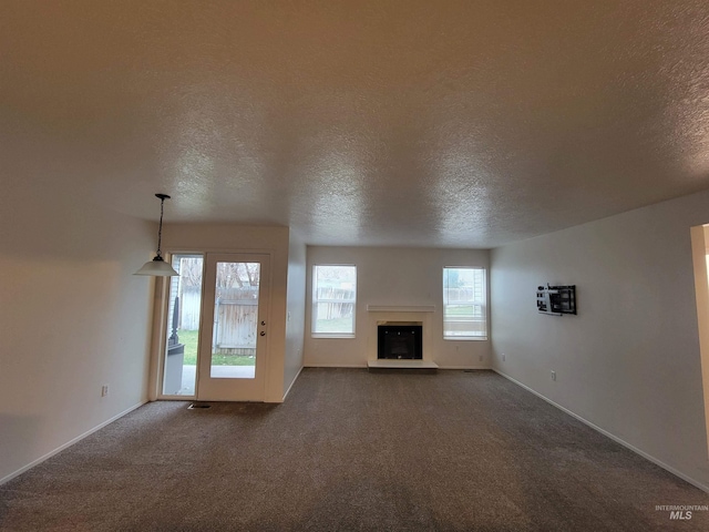 unfurnished living room featuring a fireplace with raised hearth, baseboards, dark carpet, and a textured ceiling