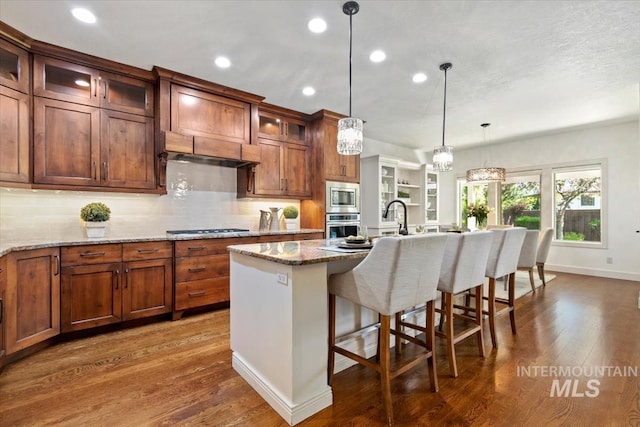 6964 N Moon Drummer Way, Meridian, ID 83646 - kitchen featuring stainless steel appliances, dark wood-style flooring, pendant lighting, a kitchen bar, and an island with sink