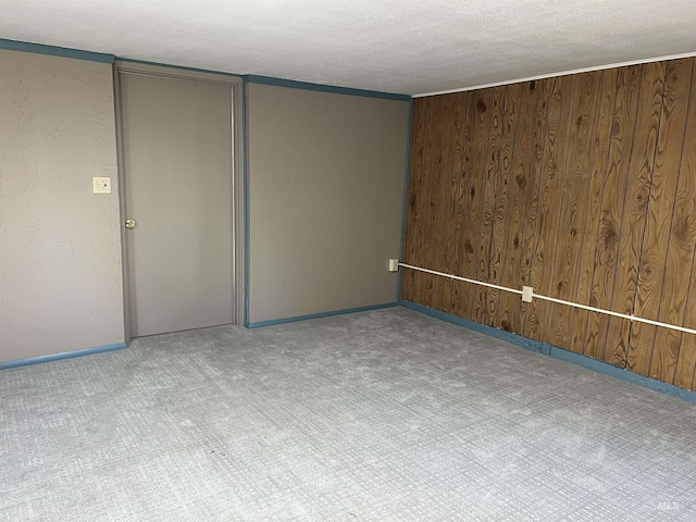 spare room featuring baseboards, wood walls, carpet, and a textured ceiling