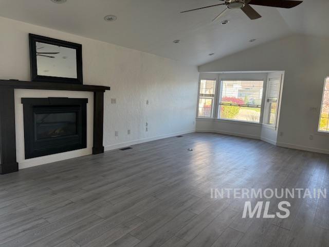 unfurnished living room featuring hardwood / wood-style flooring, vaulted ceiling, a healthy amount of sunlight, and ceiling fan