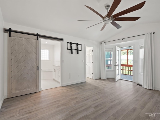 interior space featuring vaulted ceiling, a barn door, ceiling fan, and light wood-type flooring