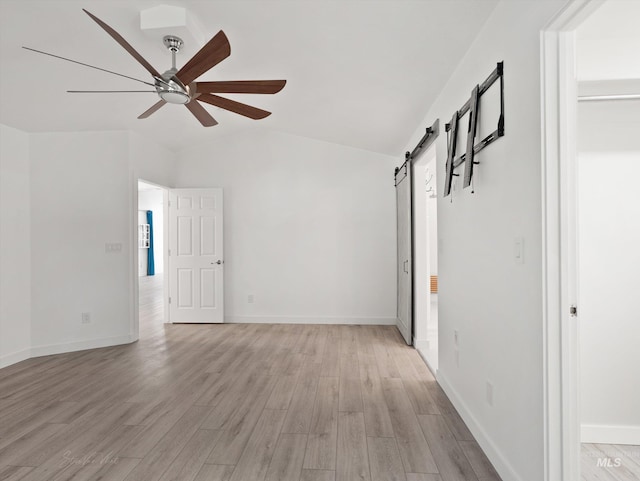 spare room featuring vaulted ceiling, a barn door, ceiling fan, and light wood-type flooring