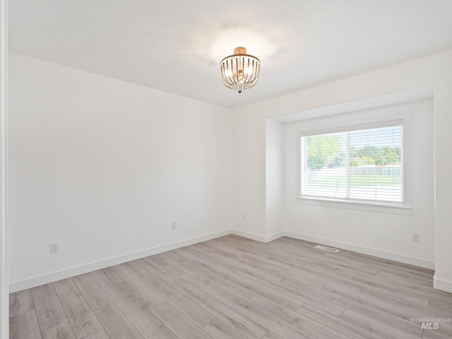 empty room with an inviting chandelier and light hardwood / wood-style flooring