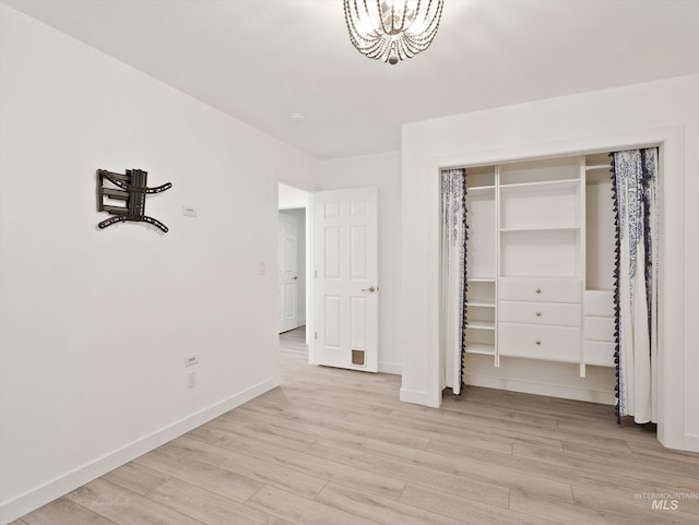 unfurnished bedroom featuring a notable chandelier, a closet, and light wood-type flooring