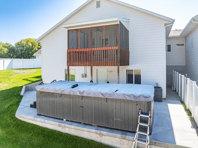 rear view of property featuring a hot tub, a patio, a sunroom, and a yard