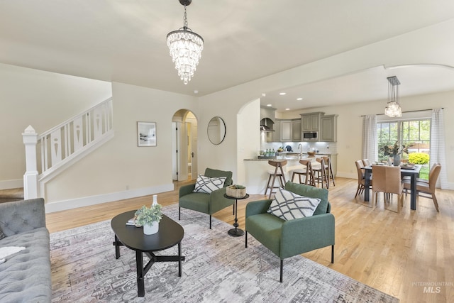 living room featuring stairs, arched walkways, baseboards, and light wood finished floors