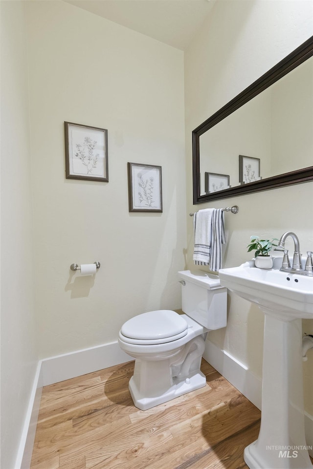half bath featuring baseboards, wood finished floors, and toilet