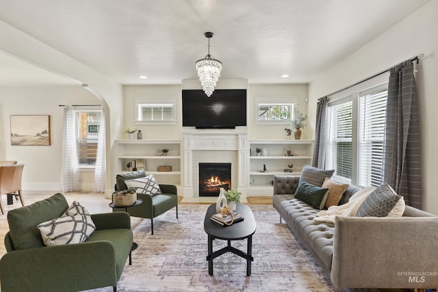 living area featuring arched walkways, baseboards, a lit fireplace, and wood finished floors