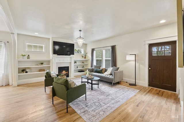 living area with light wood-type flooring, a fireplace with flush hearth, baseboards, and plenty of natural light