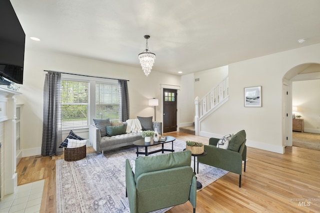 living area with an inviting chandelier, arched walkways, light wood-style flooring, and stairway