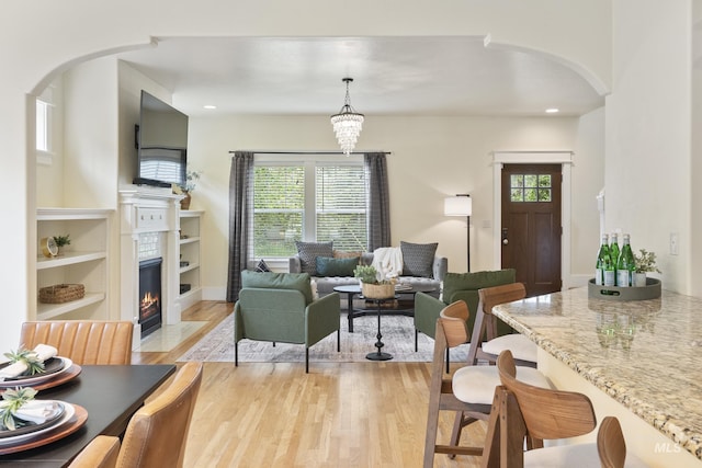 living room featuring recessed lighting, arched walkways, light wood-style flooring, and a fireplace with flush hearth