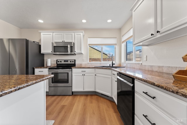 kitchen featuring a sink, white cabinetry, light wood finished floors, stainless steel appliances, and stone counters