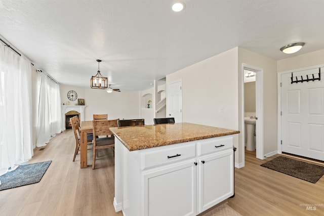 kitchen with stone countertops, light wood-style flooring, white cabinetry, a kitchen island, and pendant lighting
