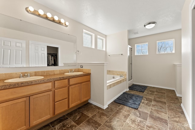 bathroom with a sink, baseboards, a shower stall, and a garden tub