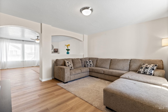 living room with ceiling fan, light wood-type flooring, arched walkways, and baseboards