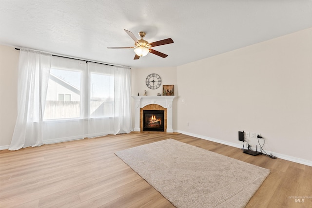 unfurnished living room featuring light wood-style flooring, ceiling fan, a fireplace, and baseboards