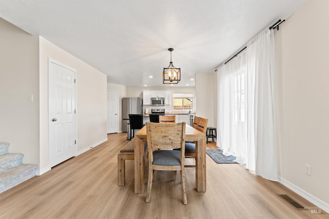 dining area with visible vents, light wood-style flooring, an inviting chandelier, and baseboards