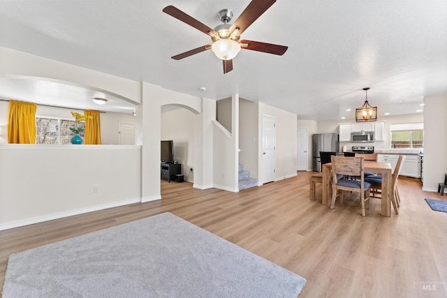 living room with baseboards, stairway, ceiling fan, arched walkways, and light wood finished floors