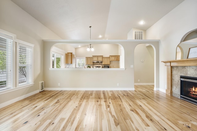 unfurnished living room with visible vents, vaulted ceiling, a tile fireplace, baseboards, and light wood finished floors
