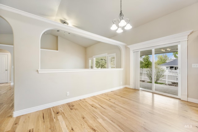 unfurnished dining area featuring arched walkways, wood finished floors, baseboards, a notable chandelier, and lofted ceiling