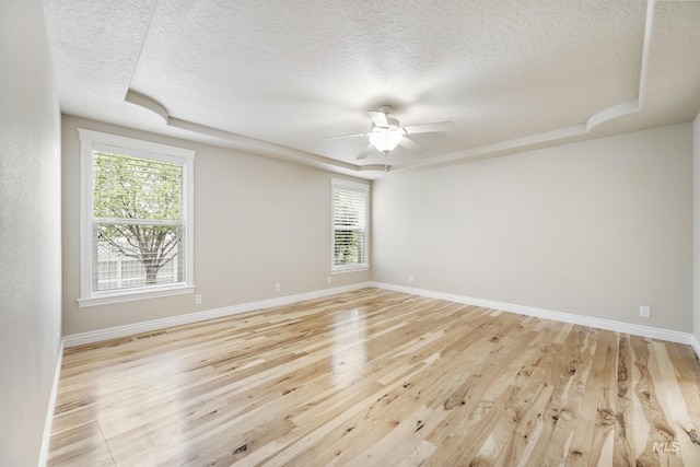 empty room featuring a ceiling fan, a textured ceiling, a raised ceiling, baseboards, and light wood-style flooring