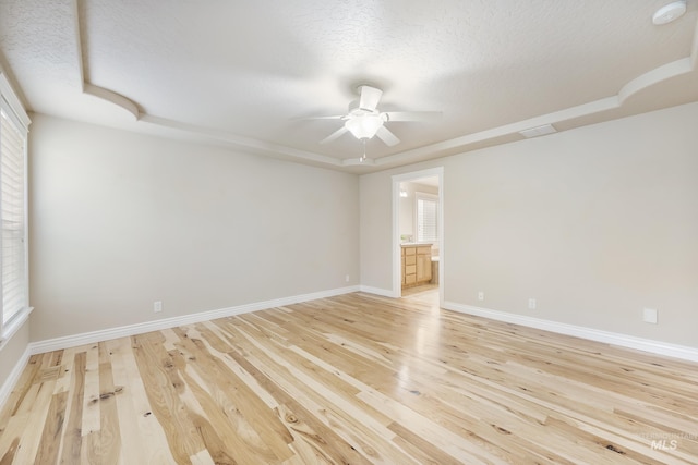 empty room with baseboards, a ceiling fan, light wood finished floors, and a wealth of natural light