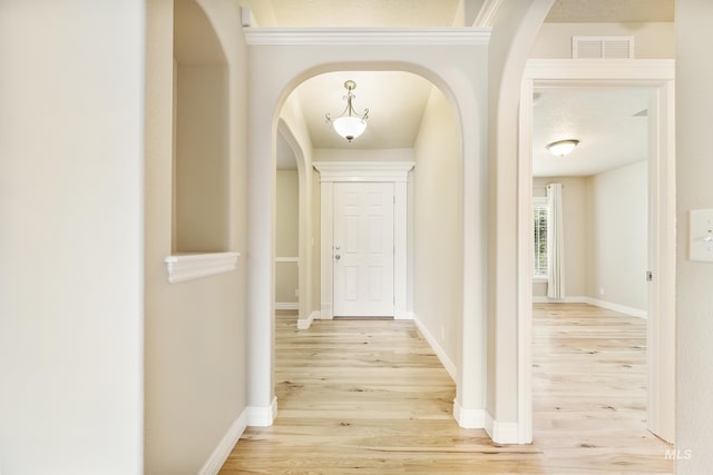 hallway with arched walkways, baseboards, wood finished floors, and visible vents