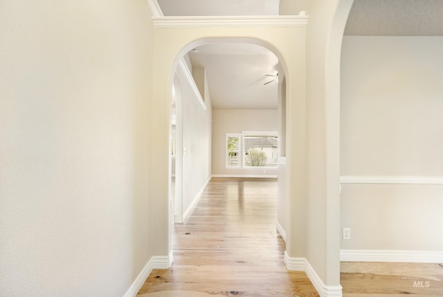 corridor featuring arched walkways, baseboards, and wood finished floors