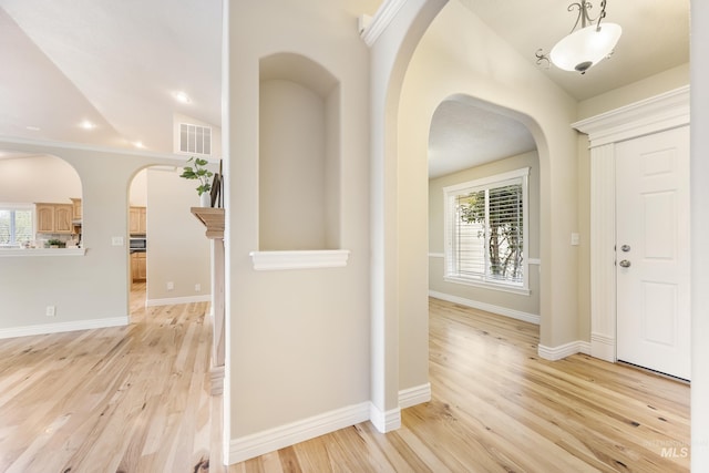 foyer with baseboards, arched walkways, light wood finished floors, and visible vents