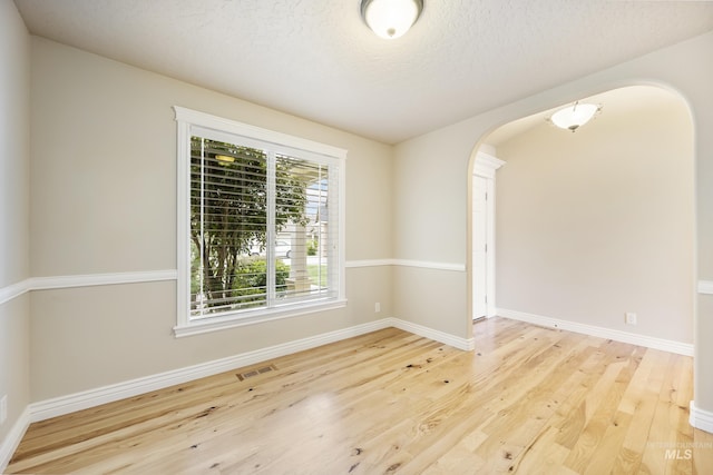 spare room with visible vents, arched walkways, baseboards, and wood finished floors