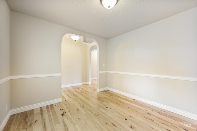 unfurnished room with arched walkways, baseboards, wood finished floors, and a textured ceiling