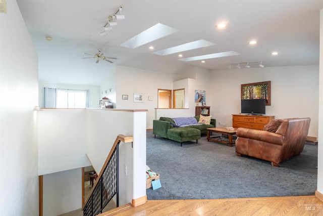 living room with ceiling fan, track lighting, wood-type flooring, and vaulted ceiling with skylight