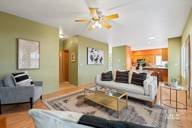 living room featuring ceiling fan, light hardwood / wood-style floors, and a textured ceiling