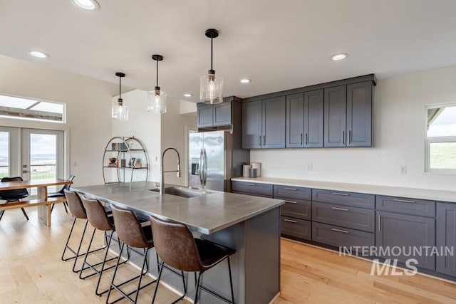 kitchen with a breakfast bar, stainless steel fridge, light wood finished floors, and a sink