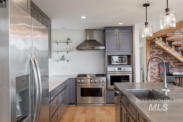 kitchen featuring wall chimney range hood, a sink, gray cabinetry, stainless steel appliances, and light wood finished floors