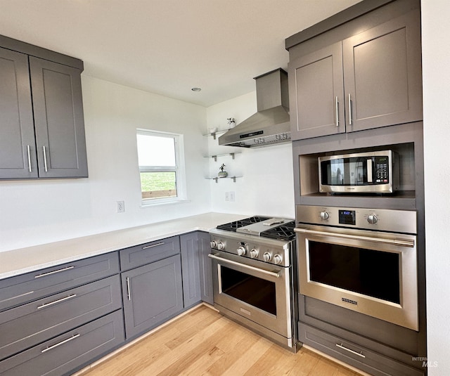kitchen with wall chimney exhaust hood, open shelves, gray cabinetry, and appliances with stainless steel finishes