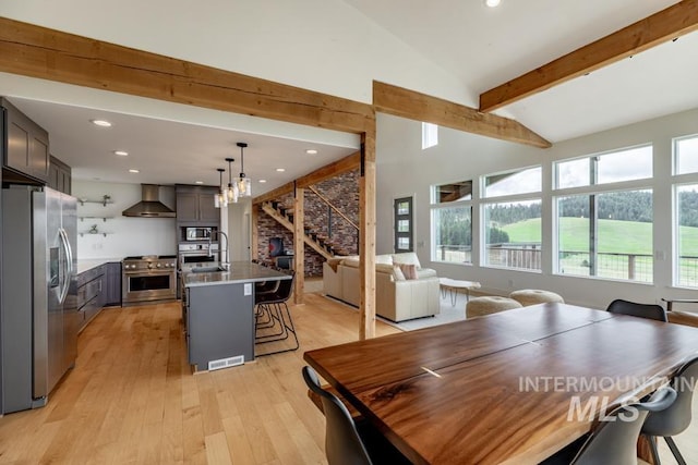 dining room with beamed ceiling, a healthy amount of sunlight, stairs, and light wood finished floors