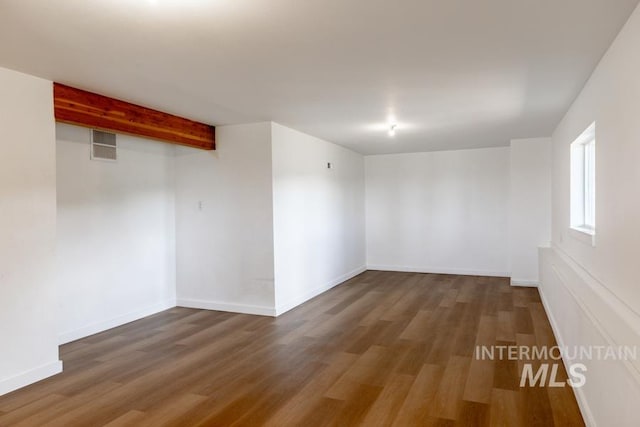 empty room featuring baseboards, visible vents, wood finished floors, and beamed ceiling