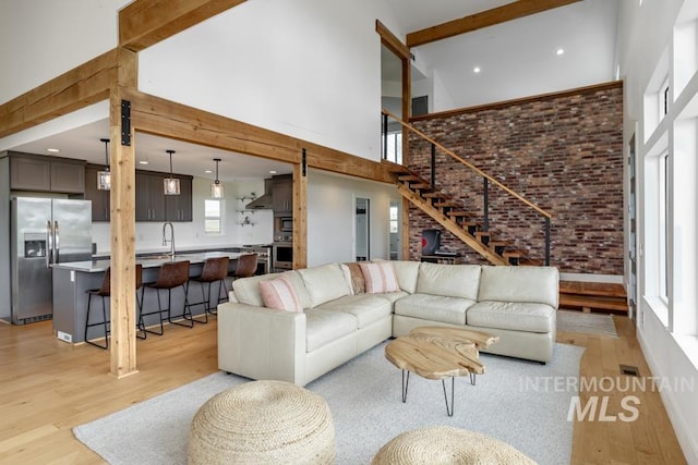 living area featuring a high ceiling, stairway, light wood-style floors, and brick wall