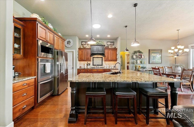 10318 W Adirondack Ct, Star, ID 83669 - kitchen featuring a sink, stainless steel appliances, brown cabinetry, a breakfast bar area, and light stone countertops