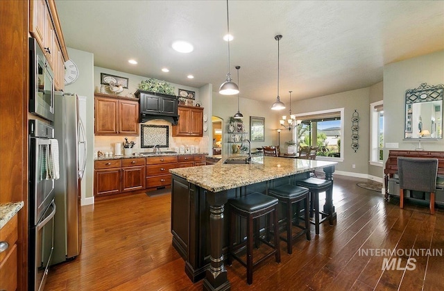 10318 W Adirondack Ct, Star, ID 83669 - kitchen with a sink, brown cabinets, dark wood finished floors, a kitchen breakfast bar, and light stone counters