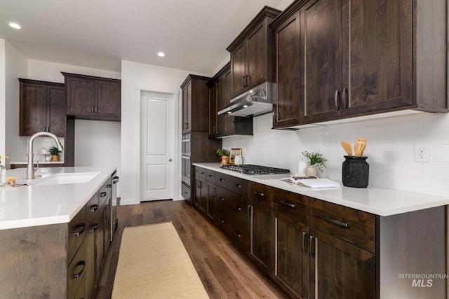 kitchen featuring under cabinet range hood, stainless steel gas cooktop, dark wood-type flooring, a sink, and decorative backsplash