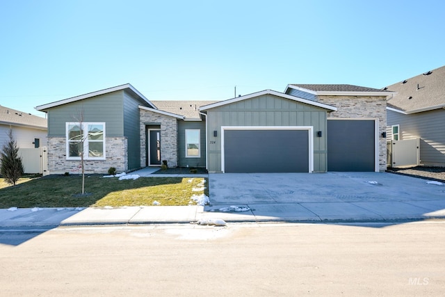 view of front of home with concrete driveway, an attached garage, board and batten siding, a front yard, and stone siding