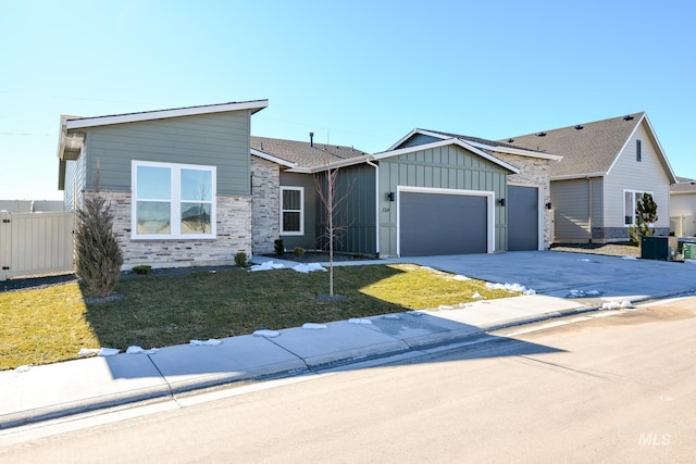 view of front of home featuring board and batten siding, a front yard, fence, a garage, and stone siding